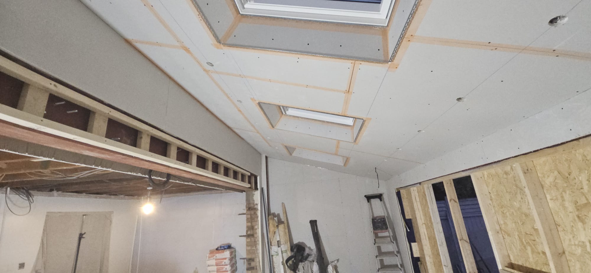 Taped plasterboard ceiling with roof windows and a steel beam over the new opening between the house and the extension